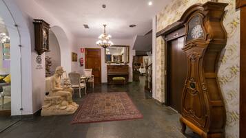 Un'ampia hall d'albergo con una grande pendola in legno, una statua, un lampadario e una tappezzeria decorata.
