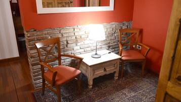 Una habitación con dos sillas de madera, una mesita blanca, una lámpara y una alfombra estampada.