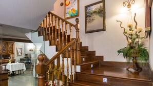 A wooden staircase with a handrail, leading to a landing with a chandelier and a framed painting. - Alda Vía León (León)