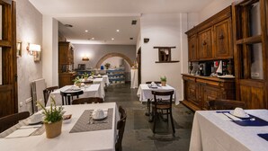 A dining area with tables set for two, wooden cabinets, and a stone floor. - Alda Vía León (León)