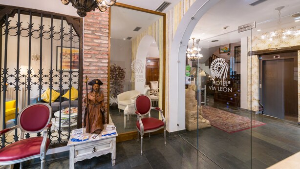 A hotel lobby with a mirror, red chairs, a statue, and a chandelier. - Alda Vía León (León)