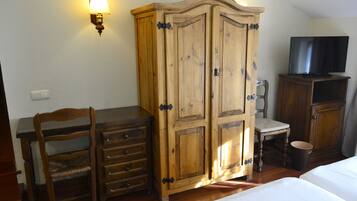 A room with a wooden wardrobe, a desk with drawers, a chair, a television, and a bed.