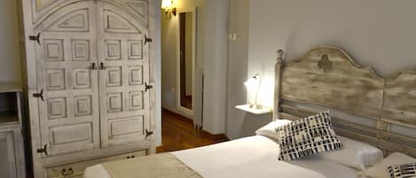 A bedroom with a large wardrobe, a bed with patterned pillows, and a nightstand with a lamp.