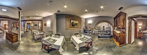 Un amplio comedor con varias mesas y sillas, una zona de bar central, y piso de piedra.