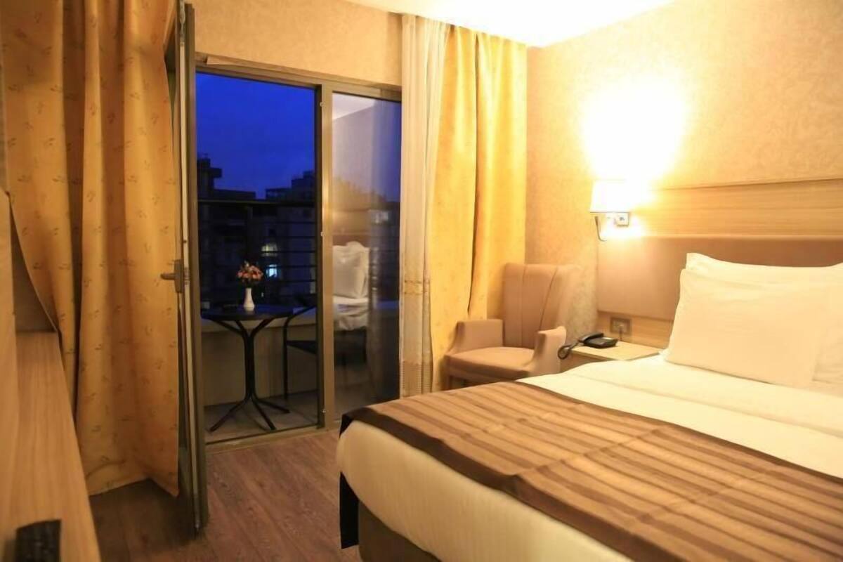 A hotel room with a bed, a chair, a table, and a sliding glass door leading to an outdoor area.