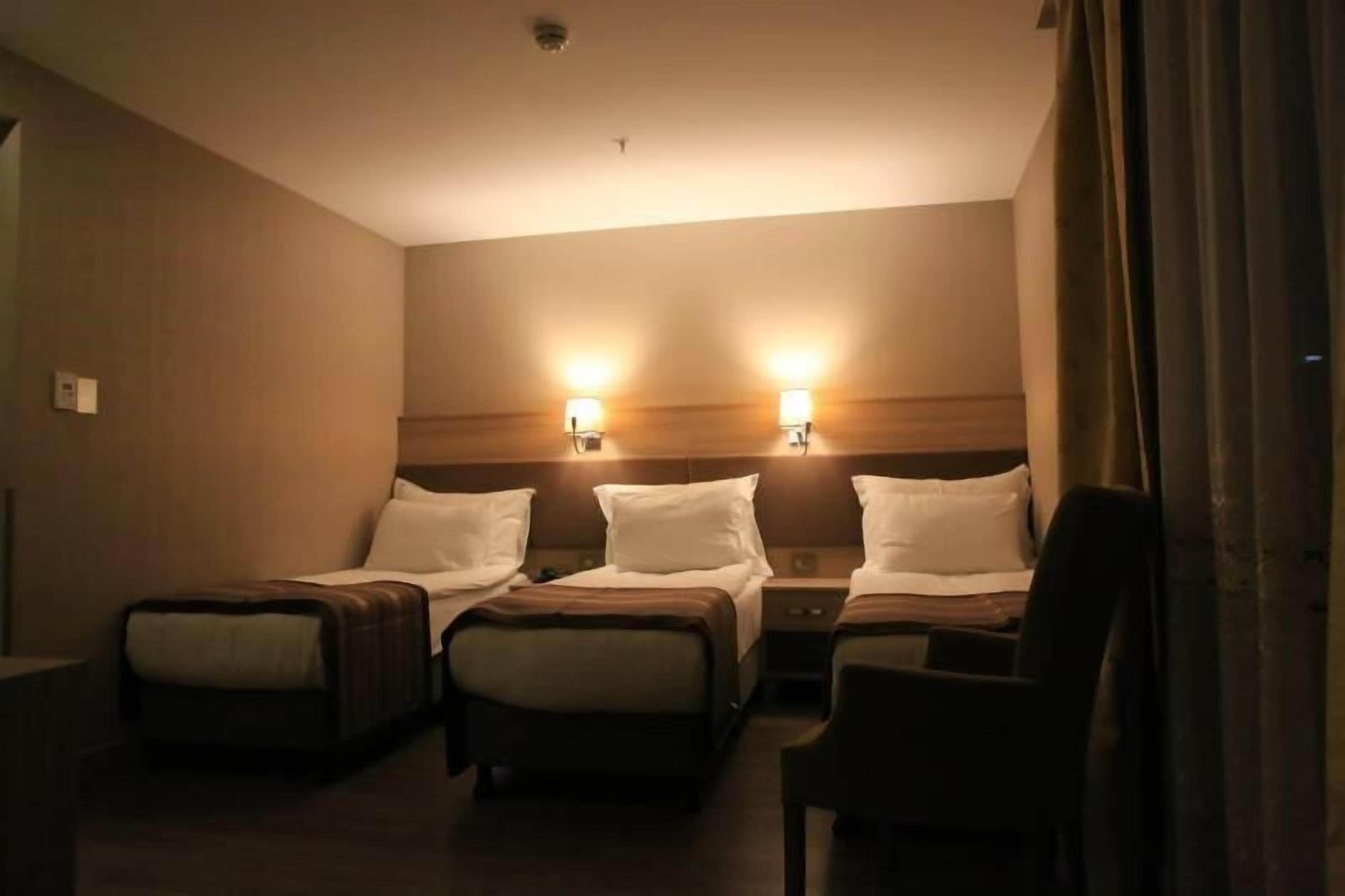 Una habitación de hotel con dos camas individuales, una silla y una mesita de noche con lámpara.