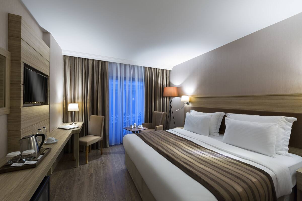 A hotel room with a bed, a desk, a chair, a TV, and a window with curtains.