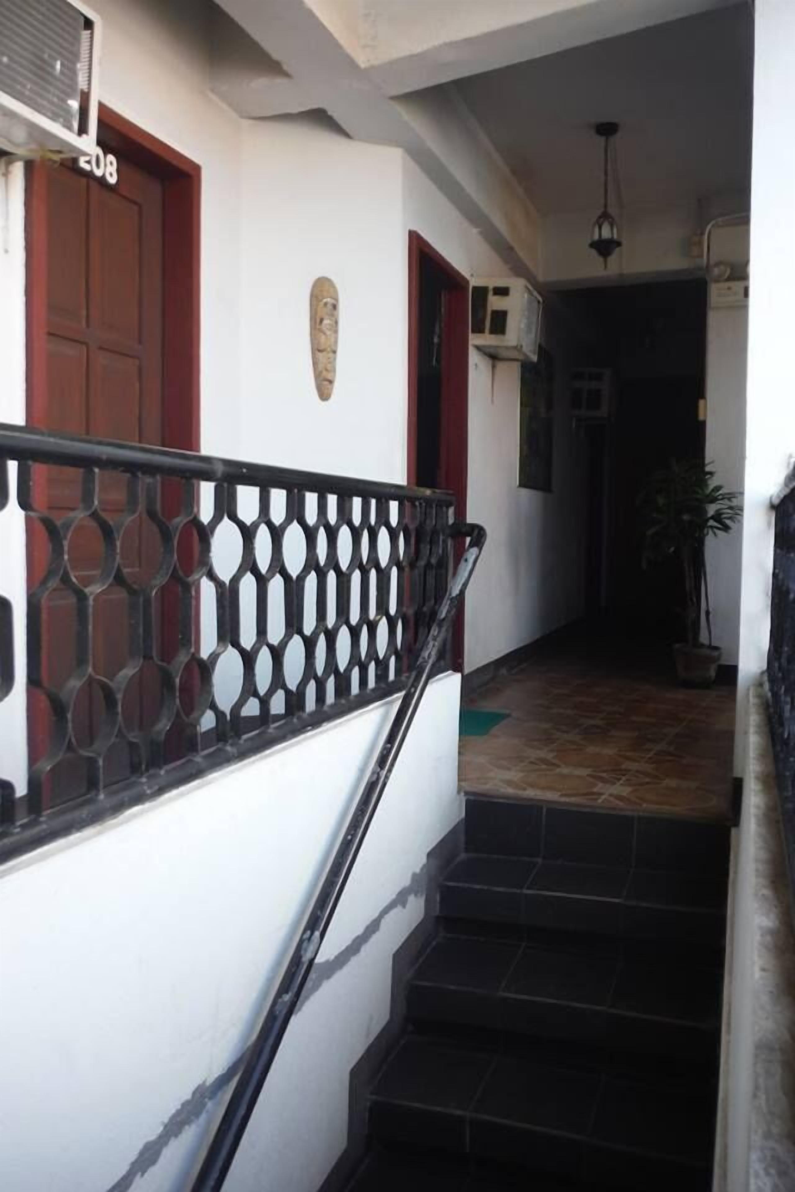 A staircase with a black metal railing, a white wall with a number '208' sign, and a potted plant in the background.