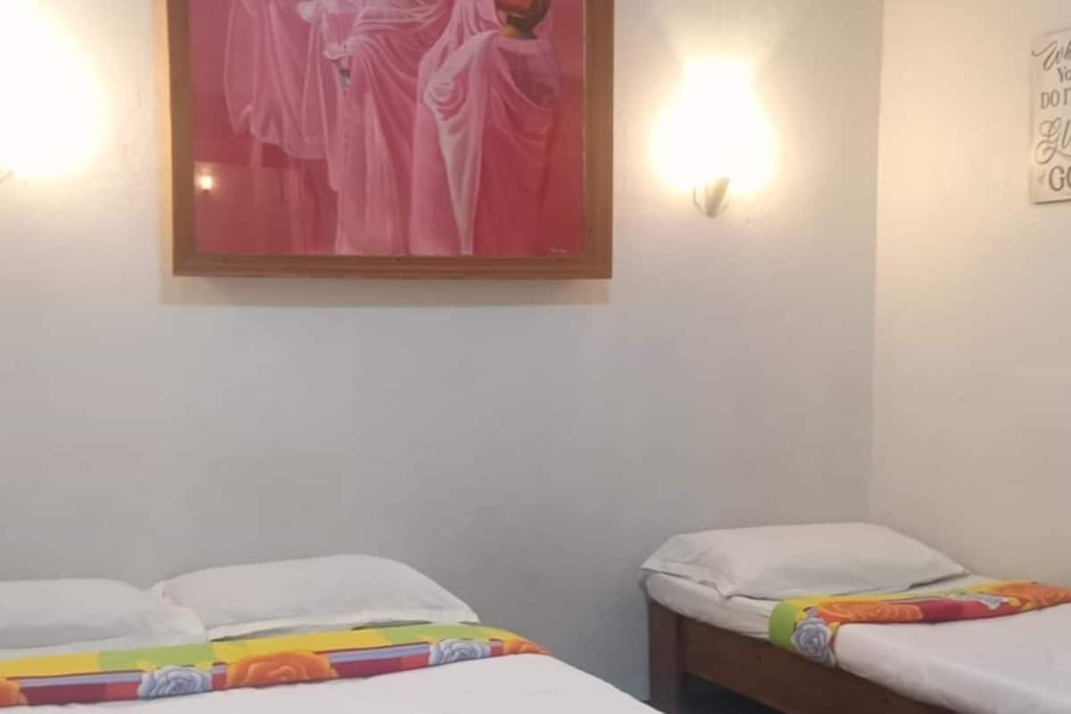 Une chambre d’hôtel avec deux lits, un tableau encadré au-dessus du lit situé à gauche, et un luminaire fixé au mur.