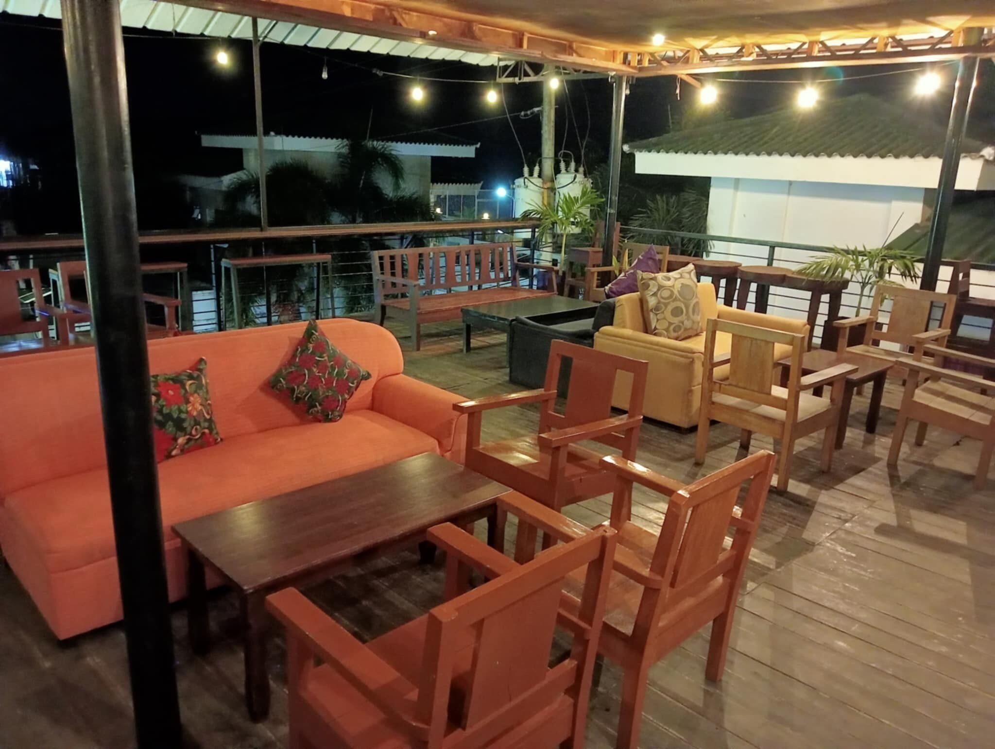 An outdoor seating area with wooden furniture, including a sofa and chairs, under a covered roof.