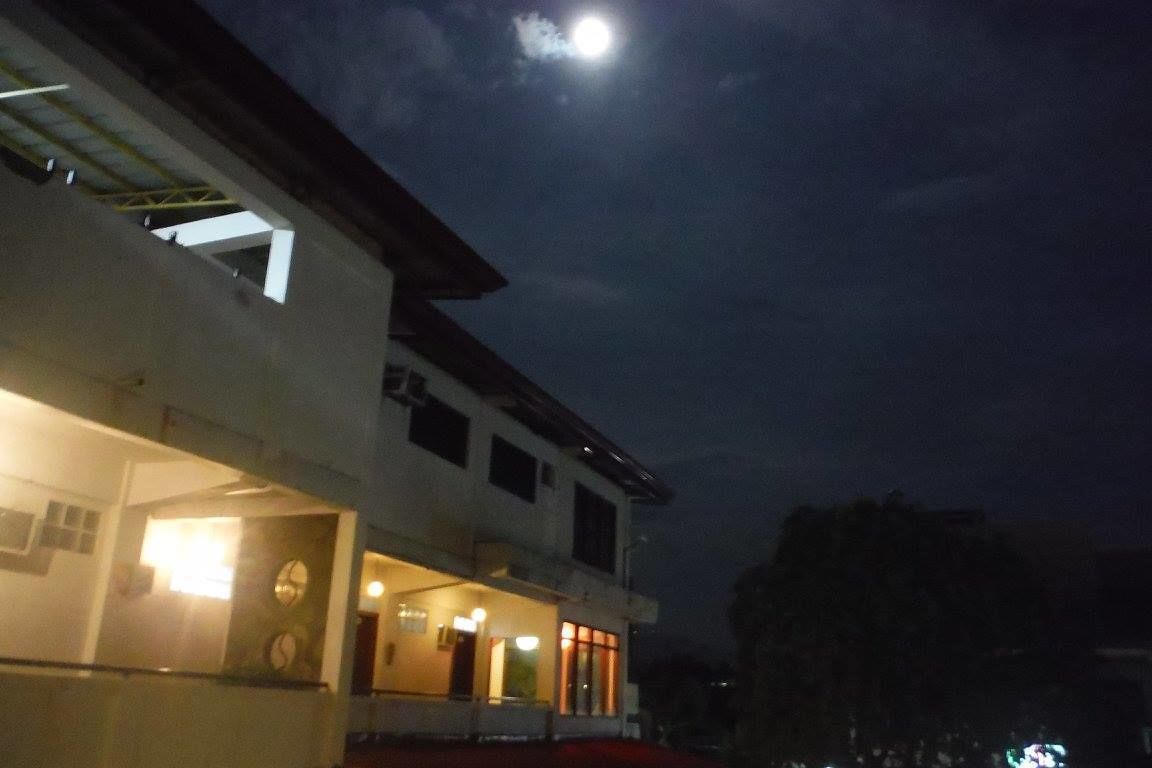 Un bâtiment doté d’un vaste espace ouvert à l’avant, qui pourrait être un hall d’entrée ou un vestibule, sous un ciel nocturne où l’on aperçoit la lune.