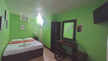 A room with green walls, a bed with a white and orange bedspread, a desk with a chair, and a mirror on the wall.
