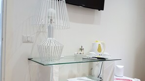 A small kitchenette with a glass-top table, a white trash bin, a white coffee machine, and a flat-screen TV mounted on the wall. - Chain Vatican Suites (Rome)