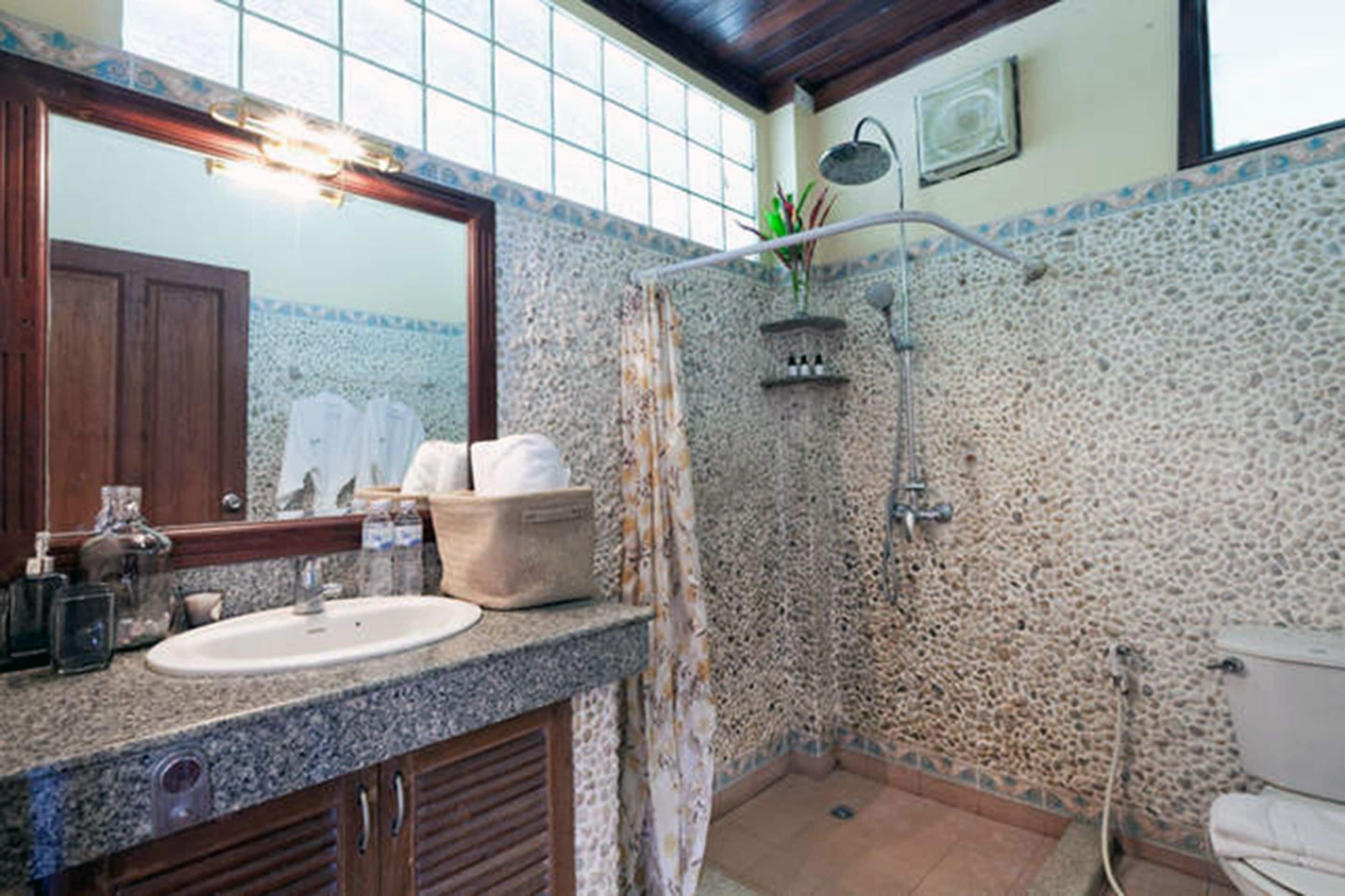 Un baño con pared de piedra, ducha, lavamanos e inodoro.
