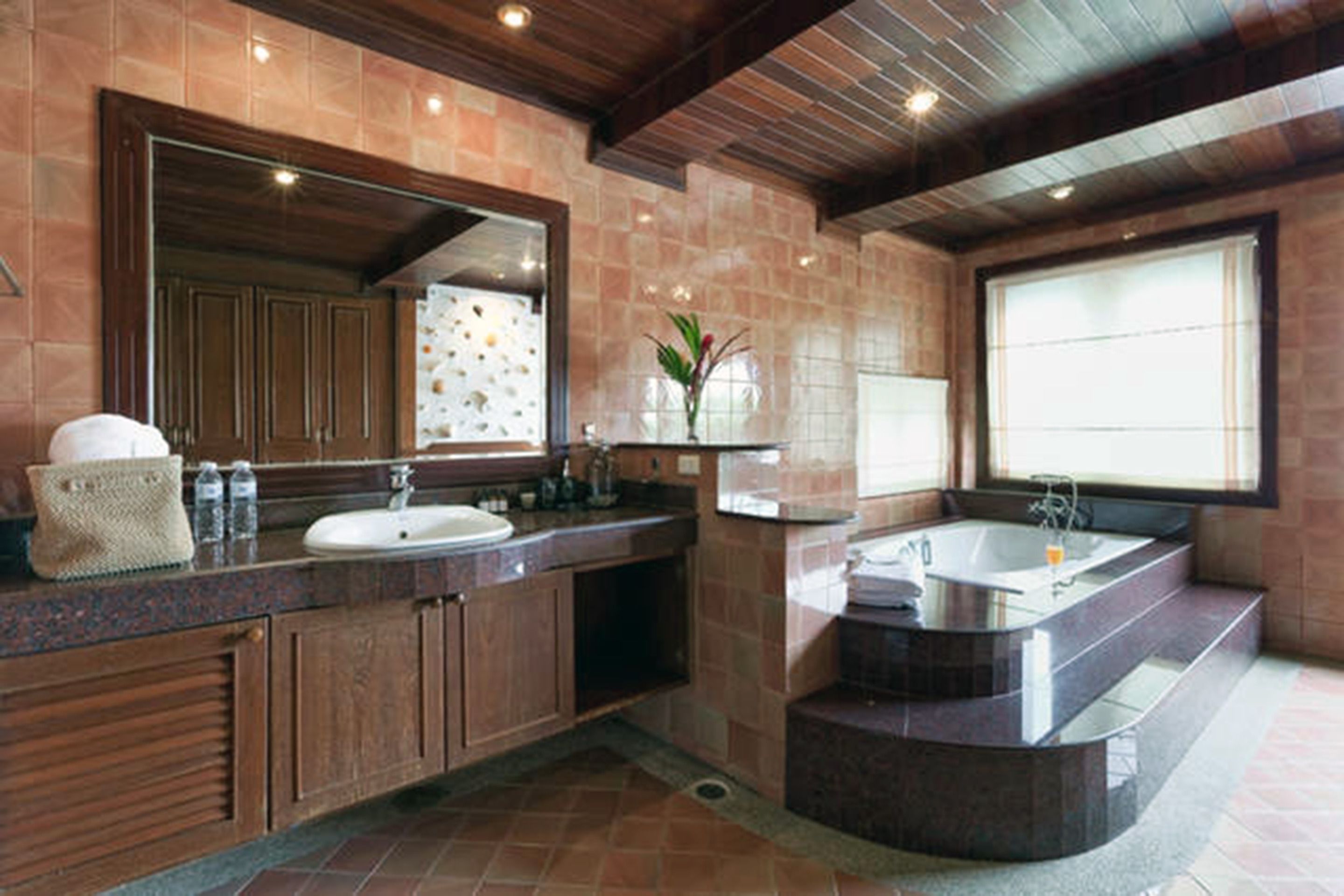 A modern bathroom with a large mirror, two sinks, a bathtub, and a window providing natural light.