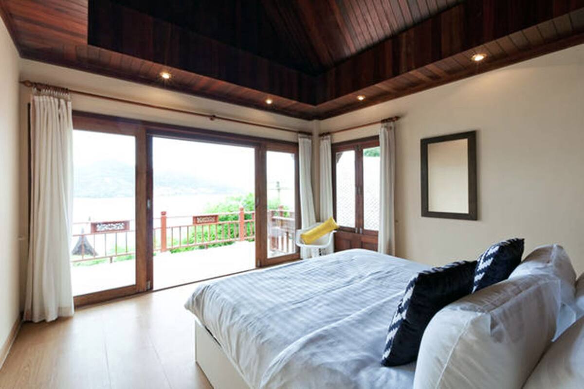 A bedroom with a large bed, wooden ceiling, and a view through the glass door.