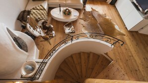Una escalera de caracol con detalles de madera, un banco blanco acolchado y una mesita con una vela y flores.