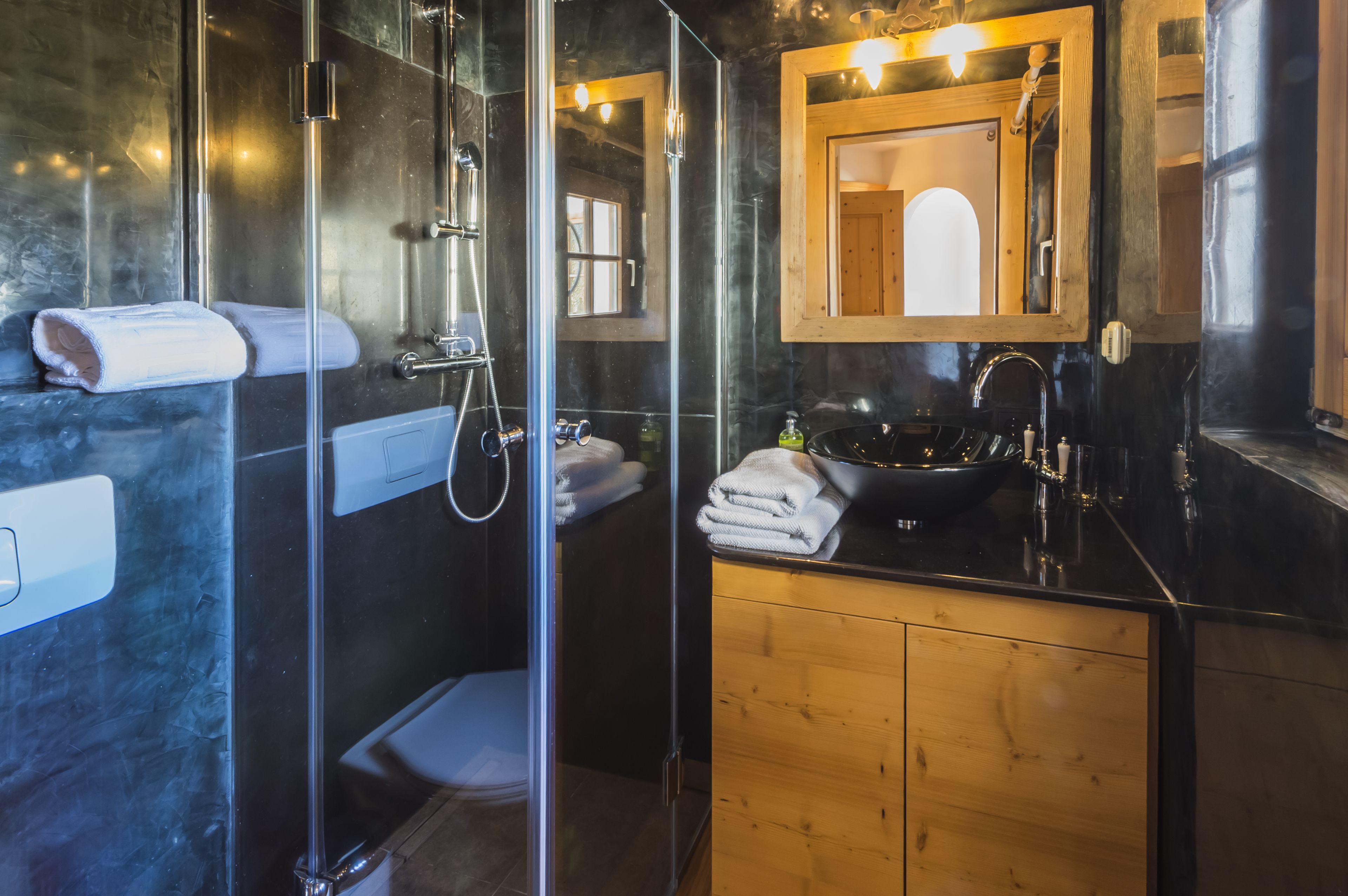 Une salle de bain moderne avec une douche à parois de verre, un meuble-lavabo en bois avec un lavabo noir et un miroir au-dessus du lavabo.