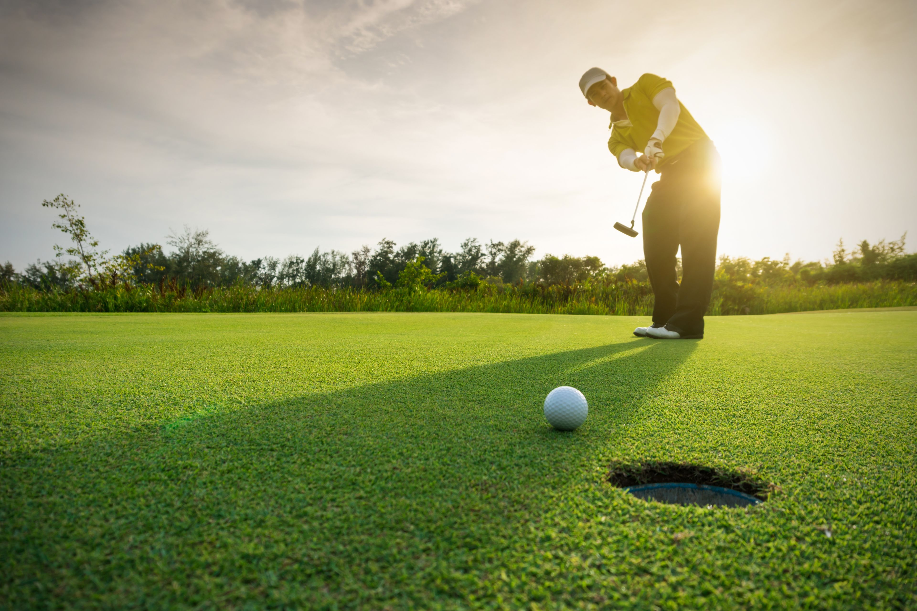 A person on a golf course preparing to putt a golf ball into a hole.
