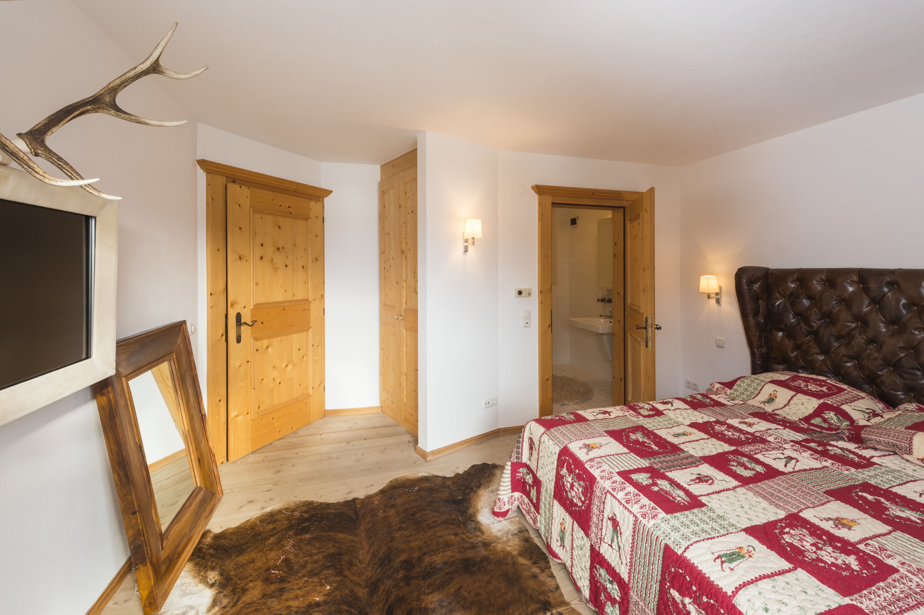 Un dormitorio con una cama grande, puertas de madera, un espejo y un par de cornamentas de ciervo.