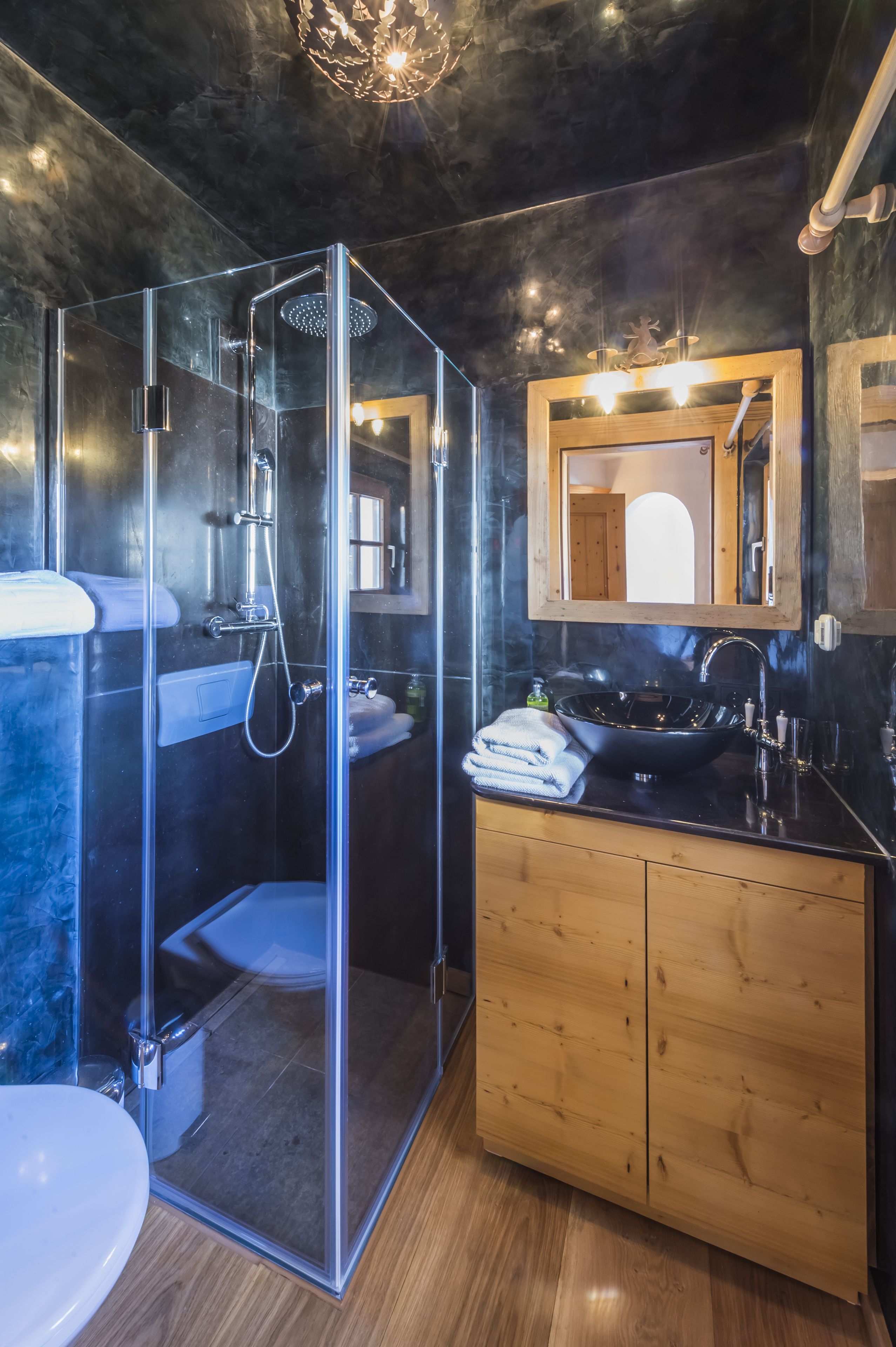 Un baño moderno con ducha de vidrio, tocador de madera y un espejo grande sobre el lavamanos.
