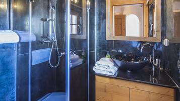 Un baño moderno con ducha de vidrio, tocador de madera y un espejo grande sobre el lavamanos.