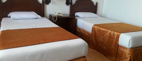 Une chambre d’hôtel avec deux lits, chacun recouvert d’une couverture marron et agrémenté d’oreillers blancs. On y trouve deux lampes fixées au mur et une table de chevet avec un téléphone.
