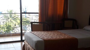 A hotel room with two beds, a balcony with a view, and a chair. - Hotel Don Felipe (Ormoc)