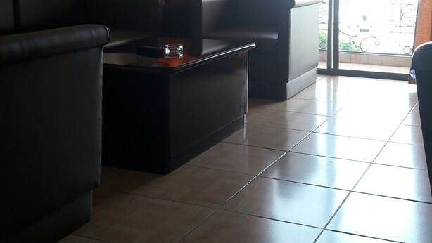 A living room with a sofa, a coffee table, and a view of a balcony with orange curtains. - Hotel Don Felipe (Ormoc)