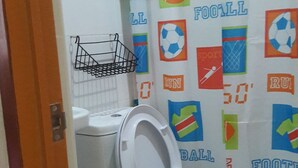 A bathroom with a toilet, a shower curtain with sports-themed designs, and a trash bin. - Hotel Don Felipe (Ormoc)