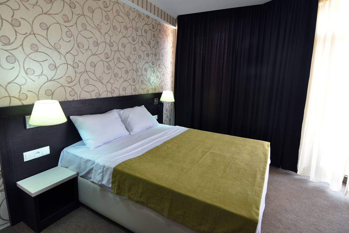 A neatly made bed with a white and green bedspread, two bedside lamps, and a nightstand with a power outlet.