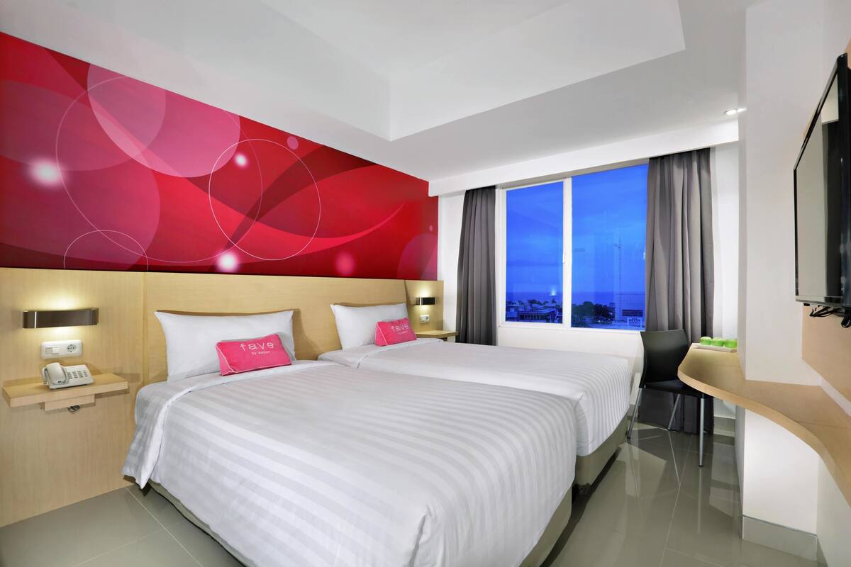 Habitación de hotel con dos camas, un escritorio, una silla, un televisor y vistas a la ciudad.
