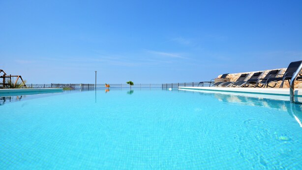A clear blue swimming pool with lounge chairs and a fence. - View 4 You Apartments (Podstrana)