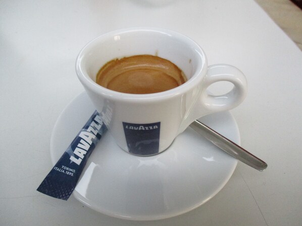 Una taza blanca de café con una cuchara y un sobre de café Lavazza a su lado.