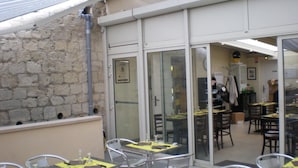 Un espace extérieur aménagé en terrasse, avec des tables et des chaises en métal, un mur en pierre et une porte vitrée donnant sur une salle à manger intérieure.