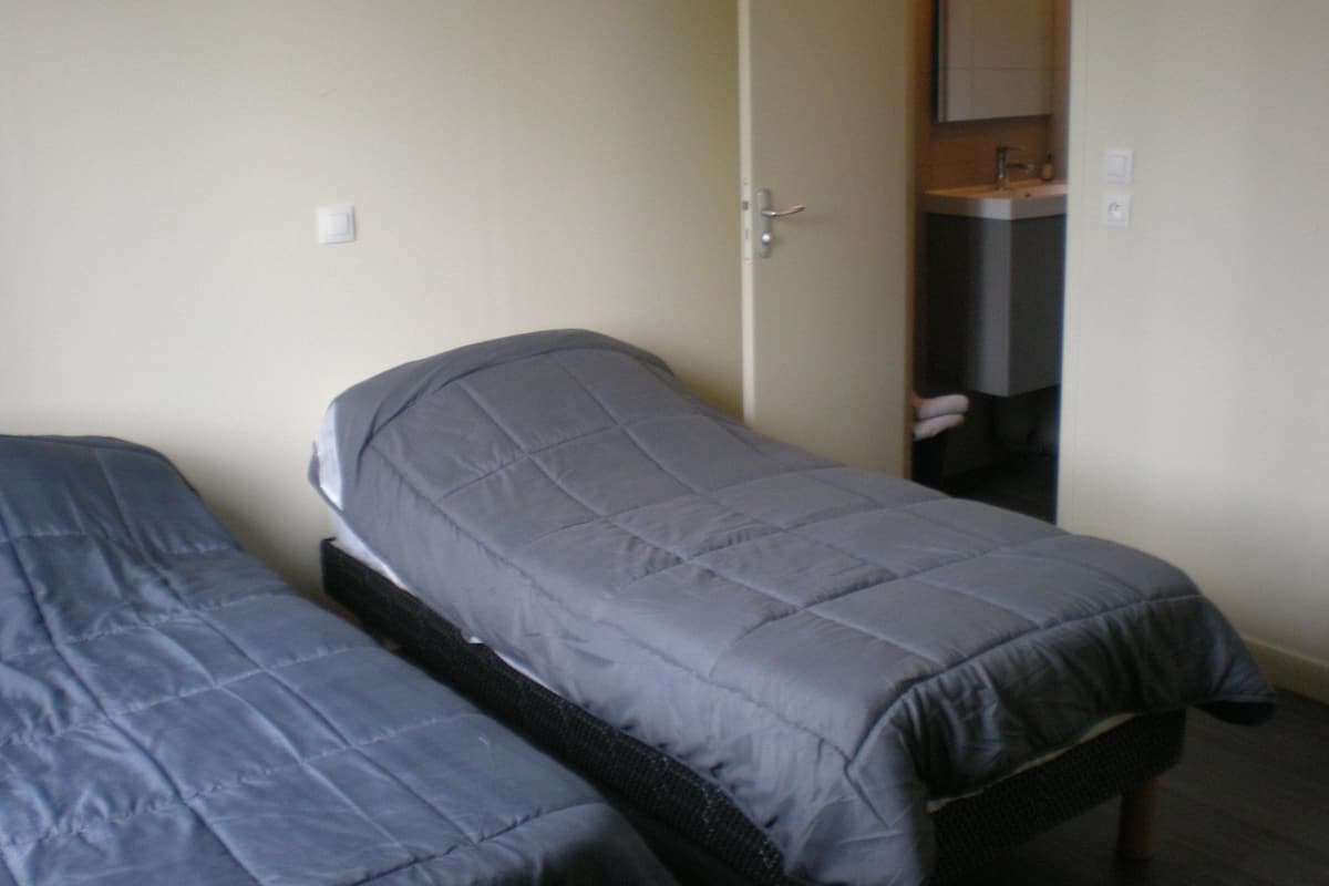 Une chambre avec deux lits simples, une porte donnant sur une salle de bain et un petit lavabo.