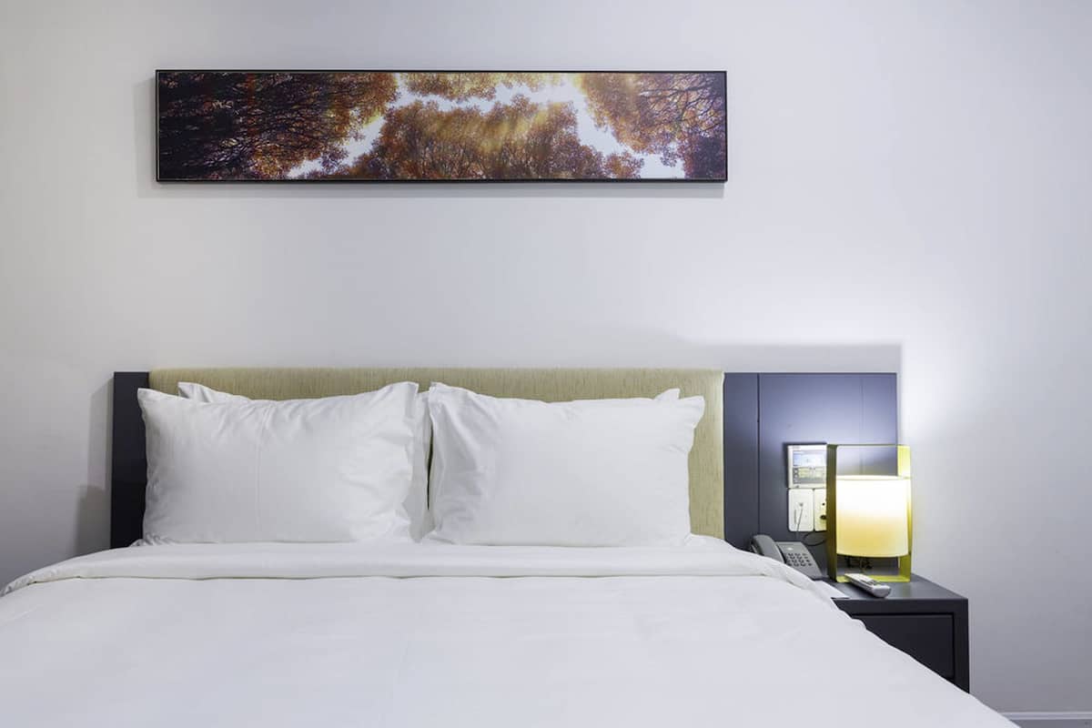 Une chambre d’hôtel avec un lit, des oreillers blancs, une table de chevet avec une lampe et un tableau au mur.