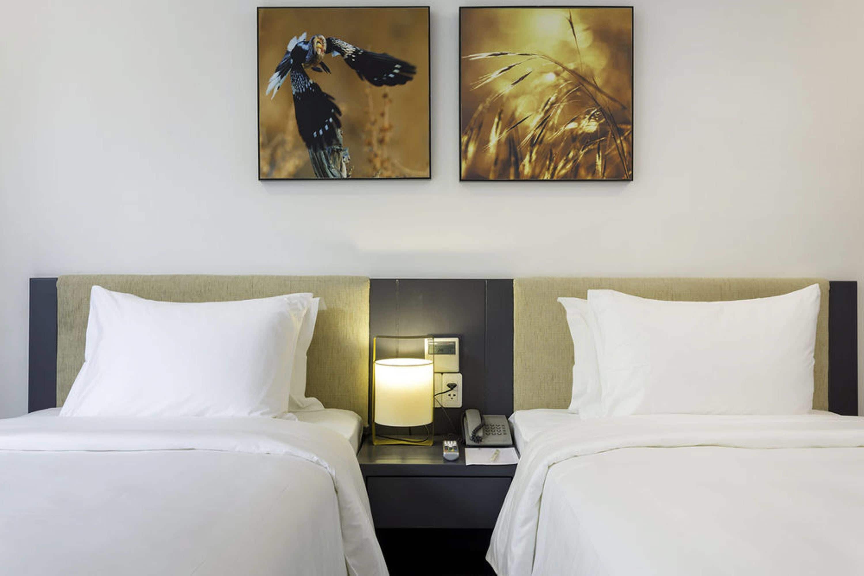 Habitación de hotel con dos camas, una mesita de noche con lámpara, teléfono y dos cuadros en la pared.