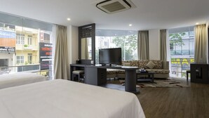 Ein Hotelzimmer mit einem großen Bett, einem Schreibtisch mit Fernseher, einer Sitzecke und einem Balkon mit Blick auf die Stadt.