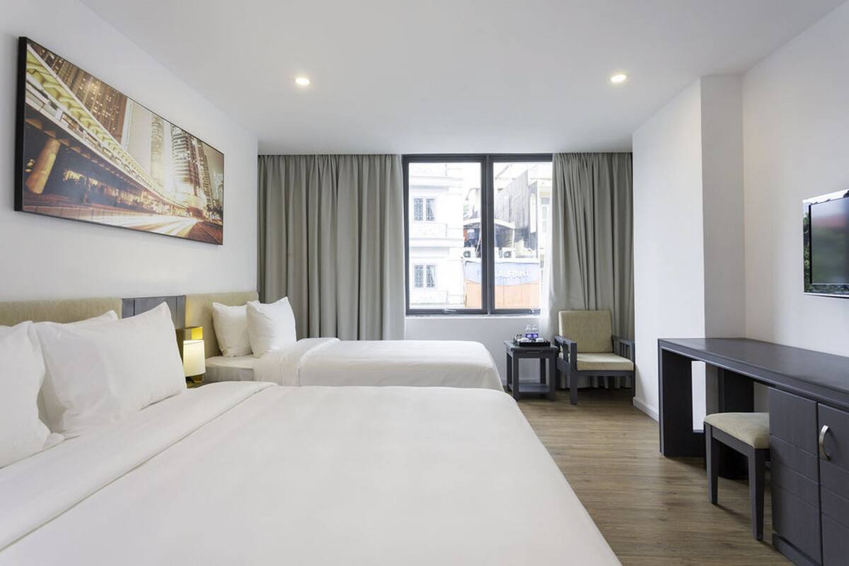 Une chambre d’hôtel avec deux lits, un bureau, une chaise, une télévision et une grande fenêtre avec des rideaux.