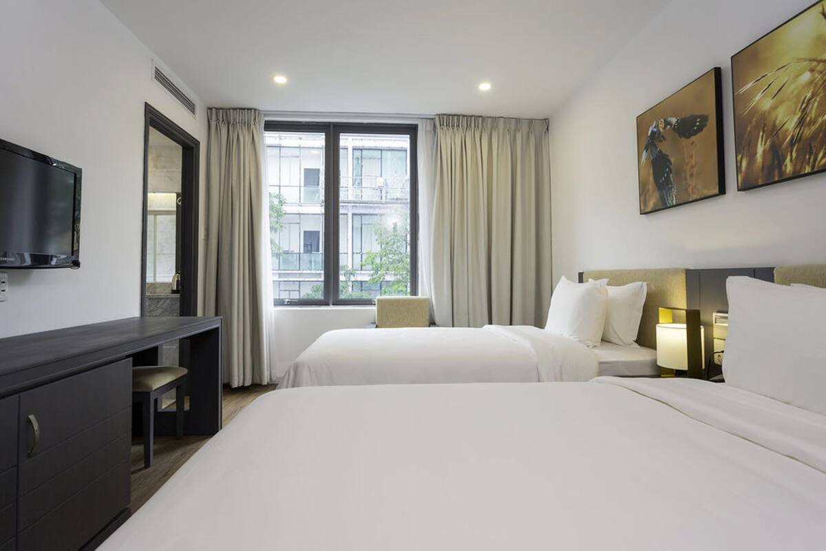 Une chambre d’hôtel avec un lit, un bureau, une chaise, une télévision et une fenêtre avec des rideaux.