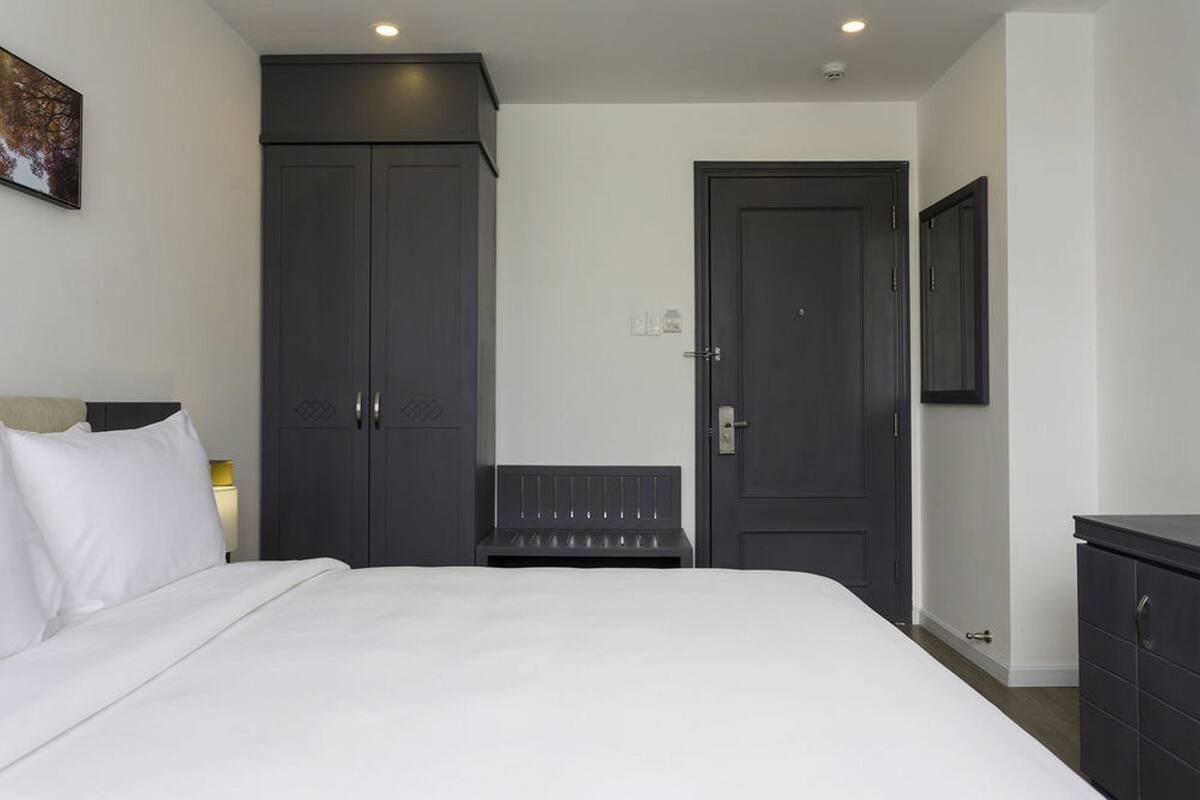 Une chambre d’hôtel avec un grand lit, une armoire en bois sombre, un banc et un téléviseur fixé au mur.