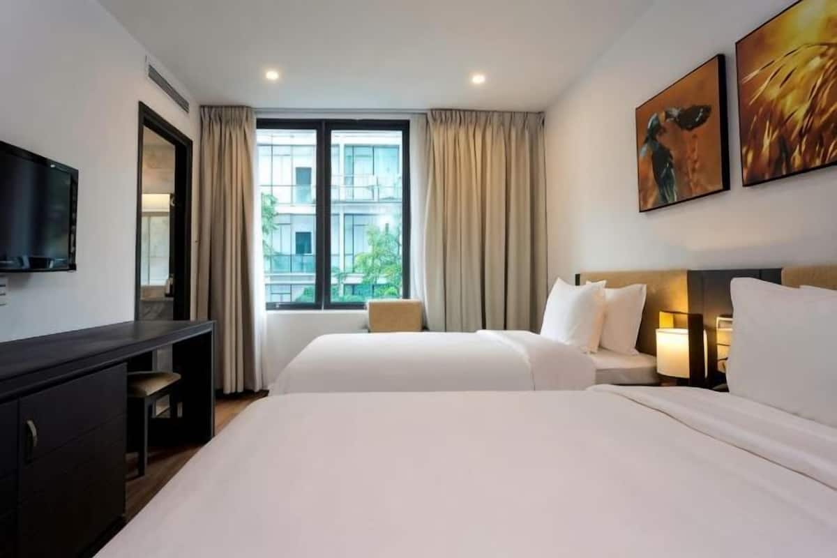 Een hotelkamer met twee bedden, een bureau, een televisie en een raam met gordijnen.