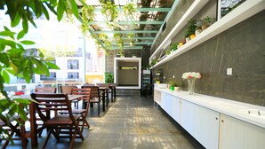 Un restaurant avec des tables et des chaises en bois, un sol en pierre et un comptoir agrémenté de plantes en pot.