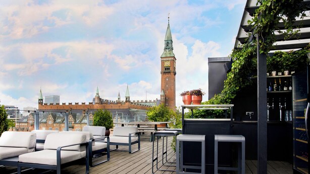 A rooftop terrace with outdoor seating, a bar area, and a view of a historic tower. - Boutique Hotel Danmark (Copenhagen)