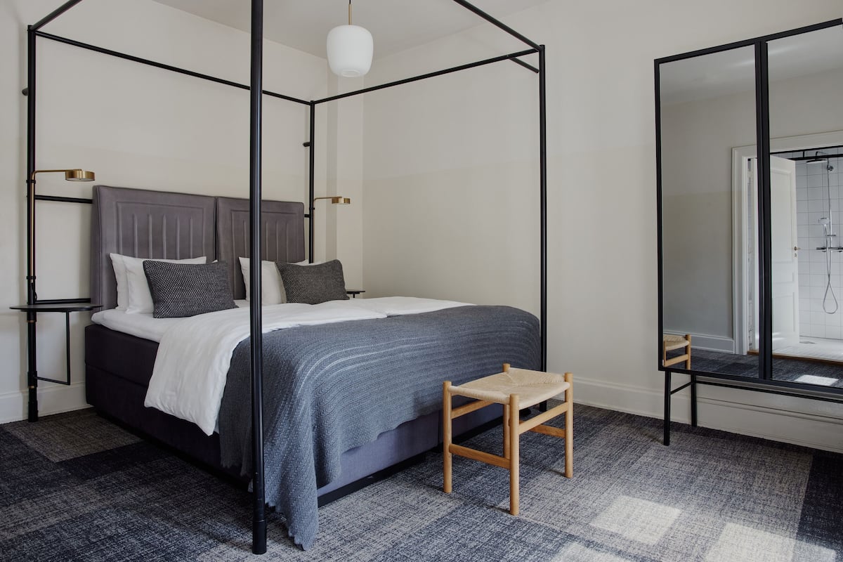 A bedroom with a four-poster bed, a small wooden stool, and a large mirror.