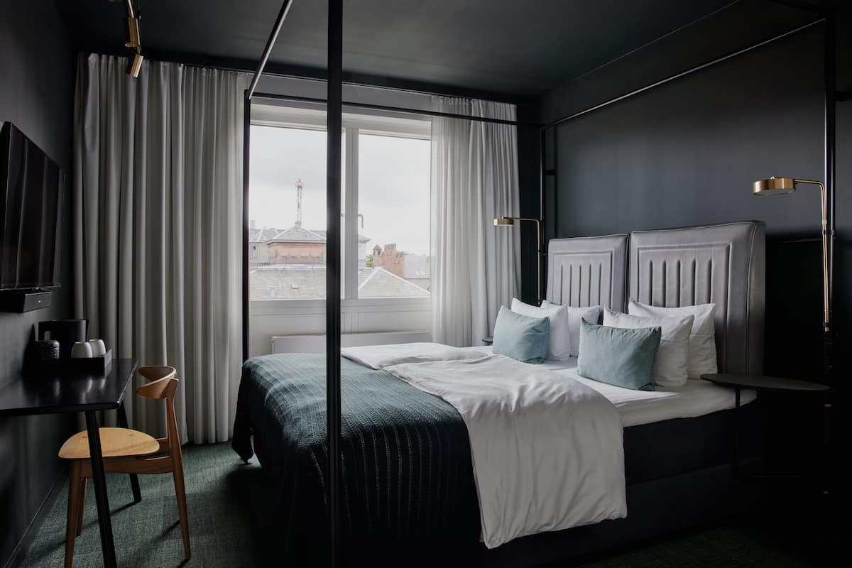 A modern hotel room with a large bed, a desk, and a chair.