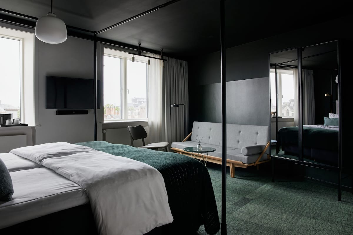 A modern hotel room with a large bed, a sofa, a small table, and a TV mounted on the wall.