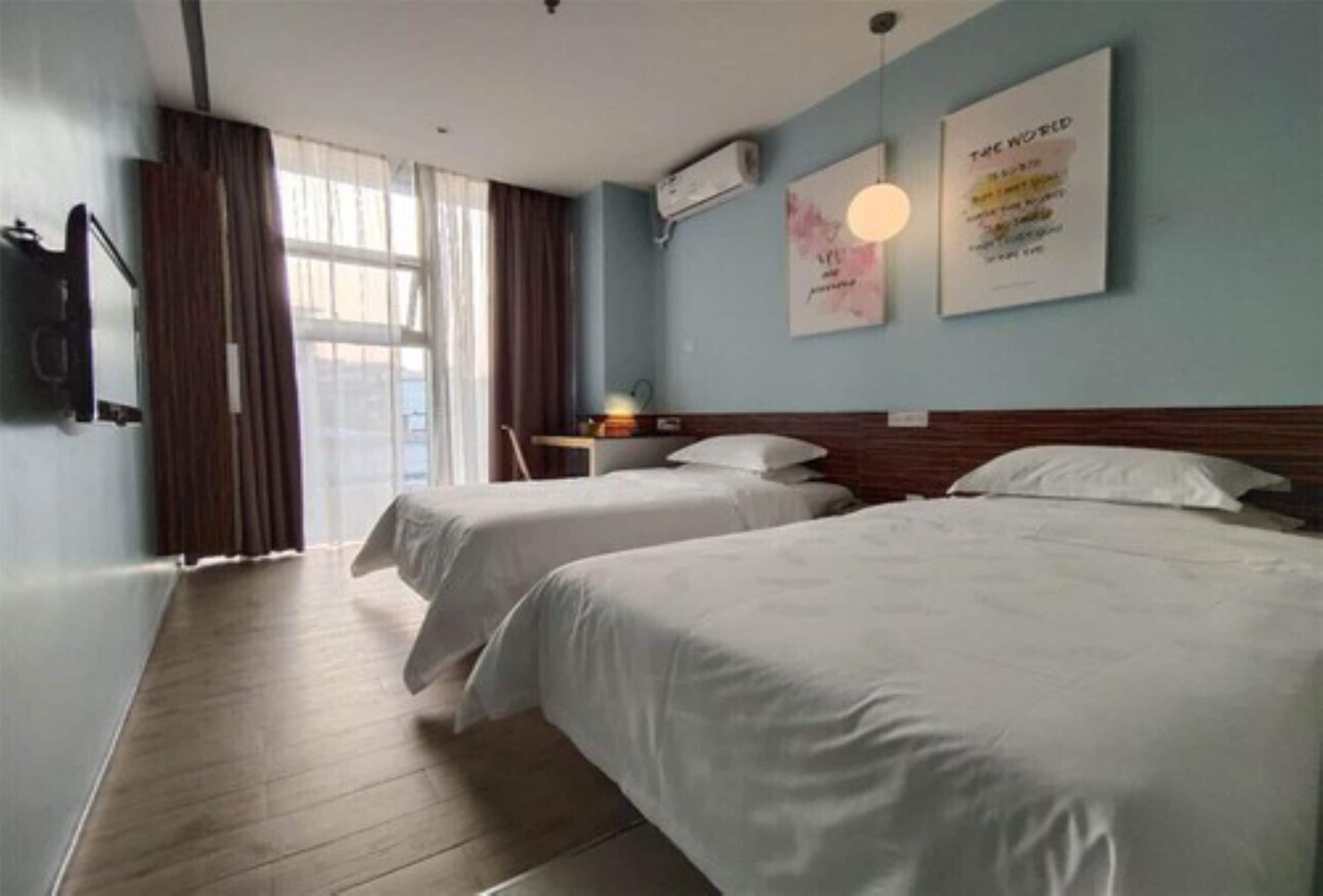 A hotel room with two beds, a TV, and a window with curtains.
