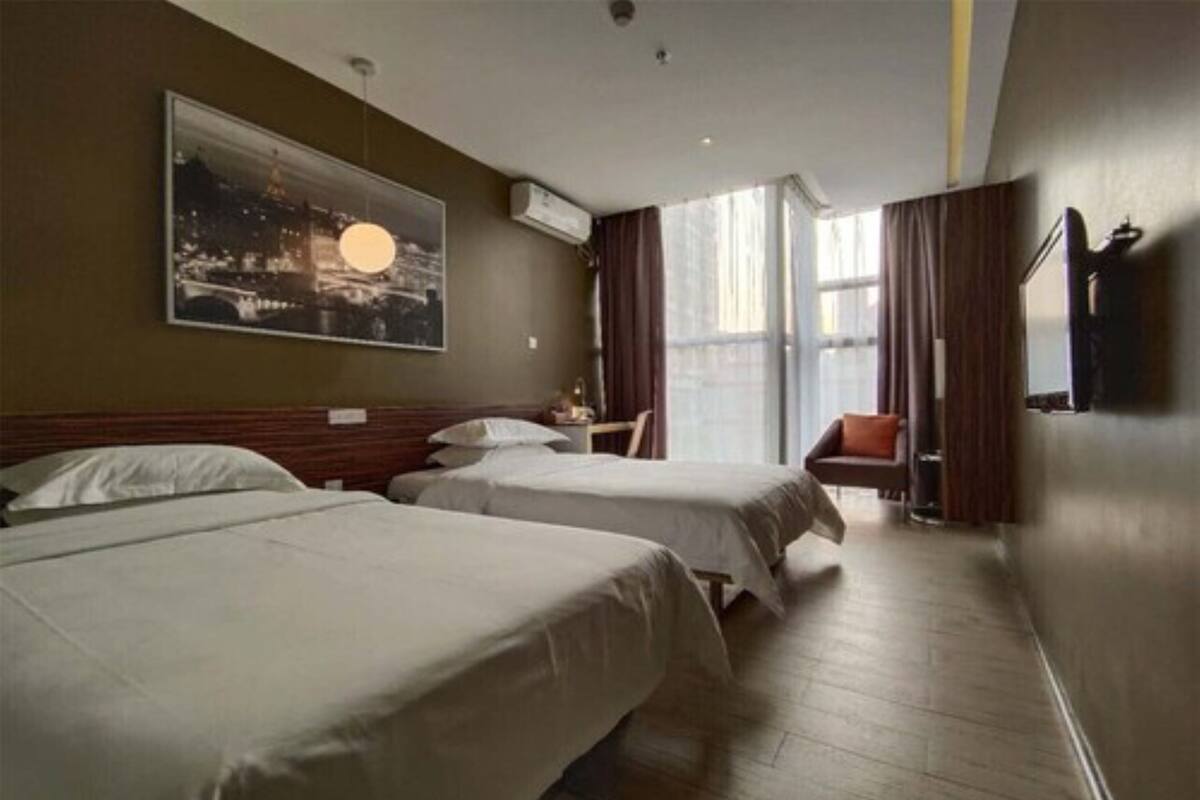 A hotel room with two beds, a large window, a chair, and a painting on the wall.